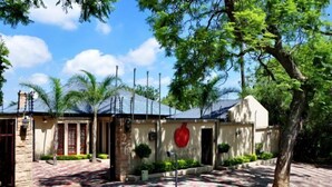 A building with a red circular sign, a stone facade, and a paved entrance area with a tree. - Red Apple Guest House (Pretoria)