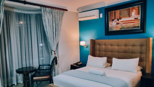 A hotel room with a bed, a chair, a desk, and an air conditioning unit. - Red Apple Guest House (Pretoria)