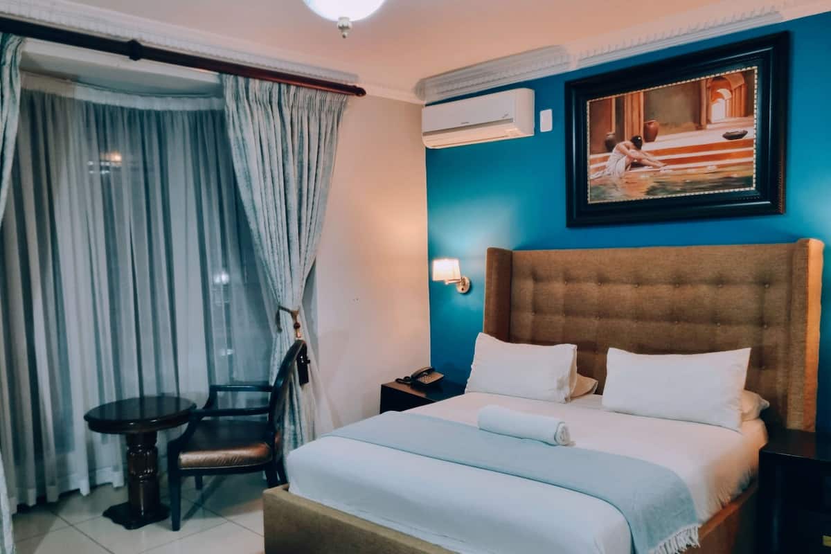 Una habitación de hotel con una cama, una silla, un escritorio y un equipo de aire acondicionado.