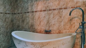 A freestanding bathtub with a faucet and a showerhead, set against a tiled wall with a decorative border. - Red Apple Guest House (Pretoria)