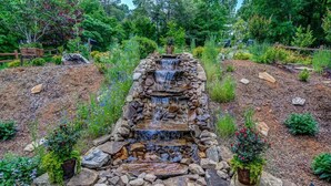 Ein mehrstufiger Steinwasserfall in einem angelegten Garten mit umgebender Vegetation und einem Holzzaun.