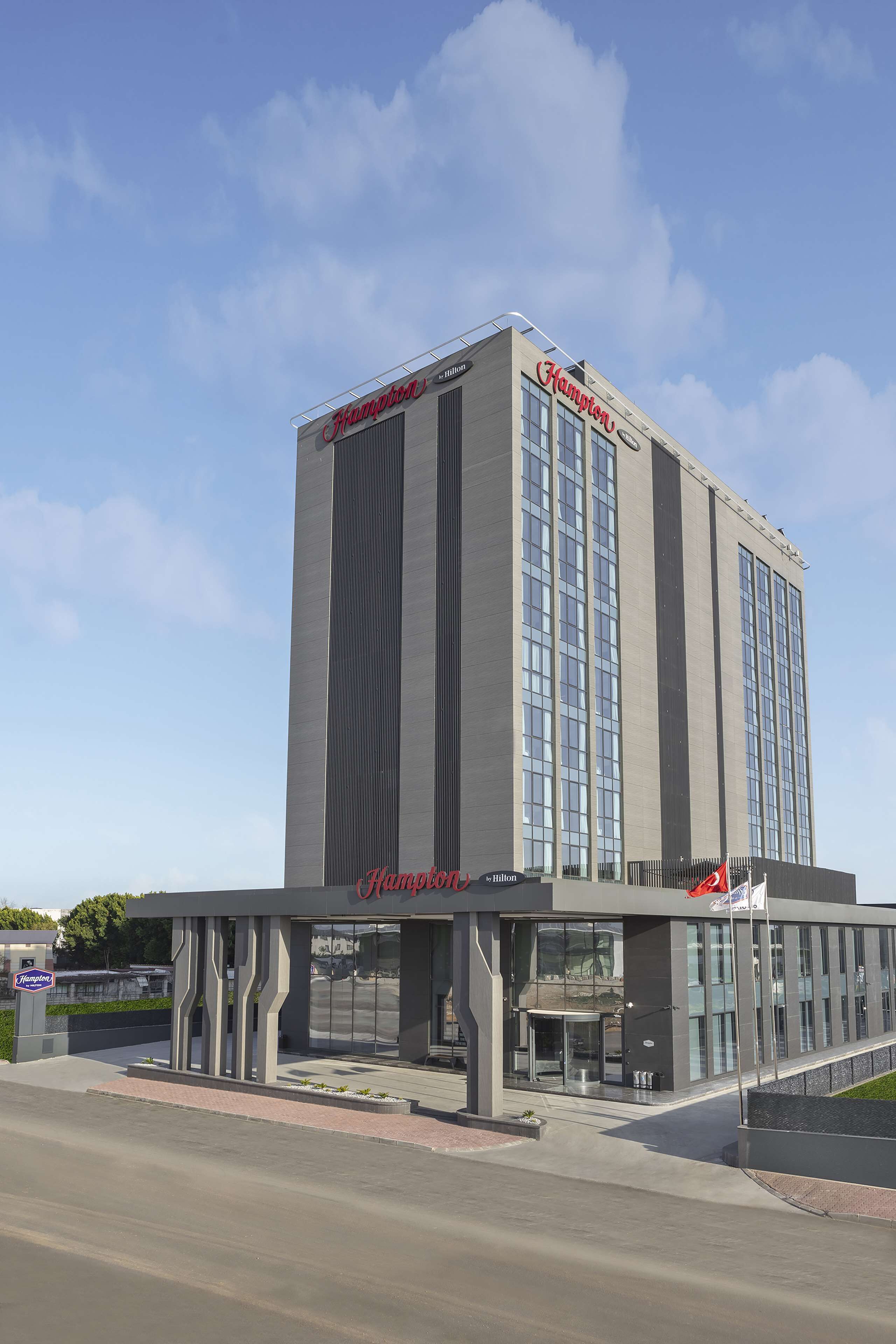 A modern hotel with a prominent 'Hampton' sign, large windows, and a covered entrance area.