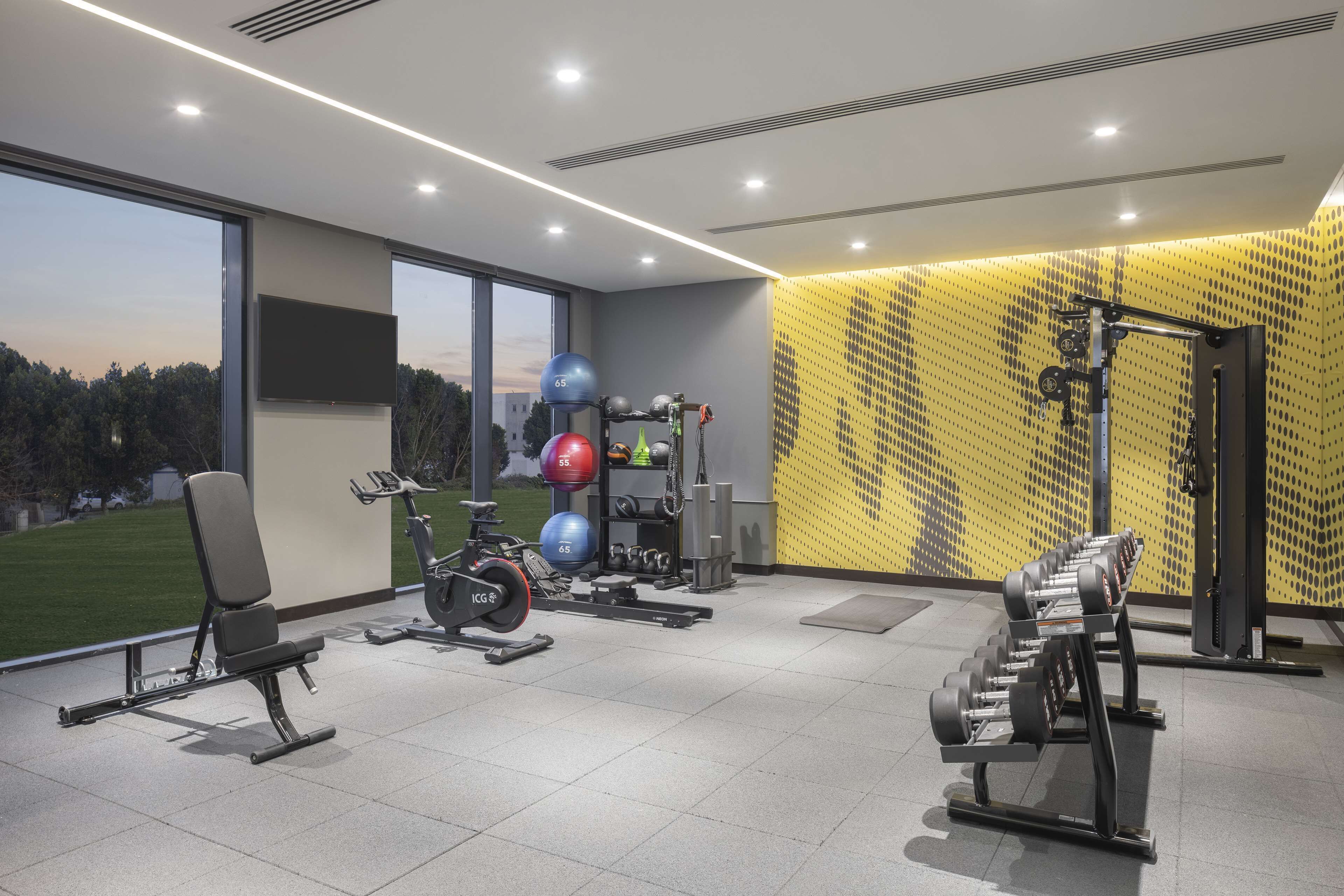 Een moderne sportschool met fitnessapparatuur, grote ramen en uitzicht op het buitengebied.