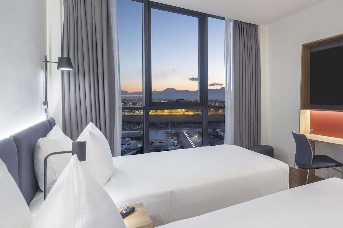 Een hotelkamer met twee bedden, een televisie en uitzicht op een stadsbeeld.