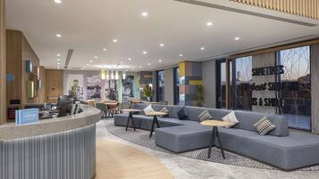 Een moderne hotel lobby met een gebogen receptiebalie, een zithoek met banken en tafels, en een groot raam met uitzicht op de skyline.