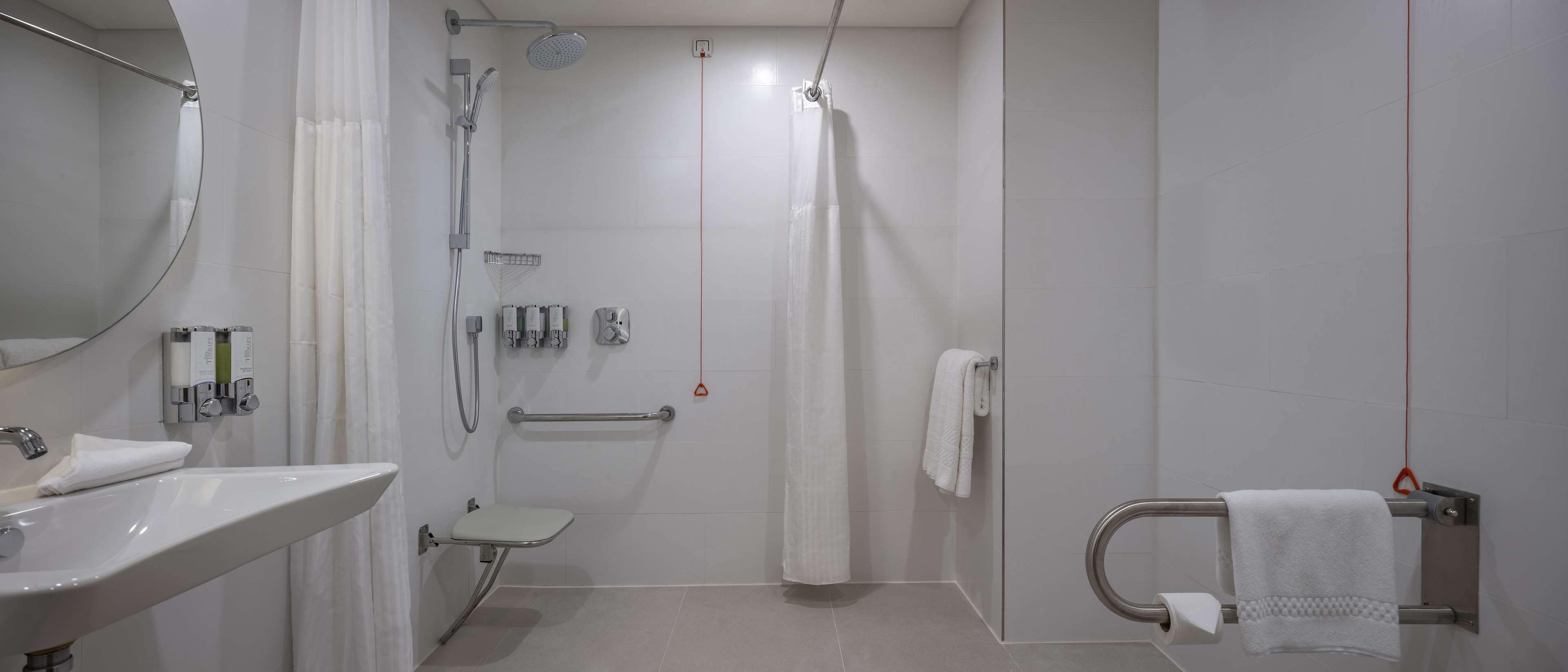 A modern bathroom with a sink, toilet, shower, and grab bars.