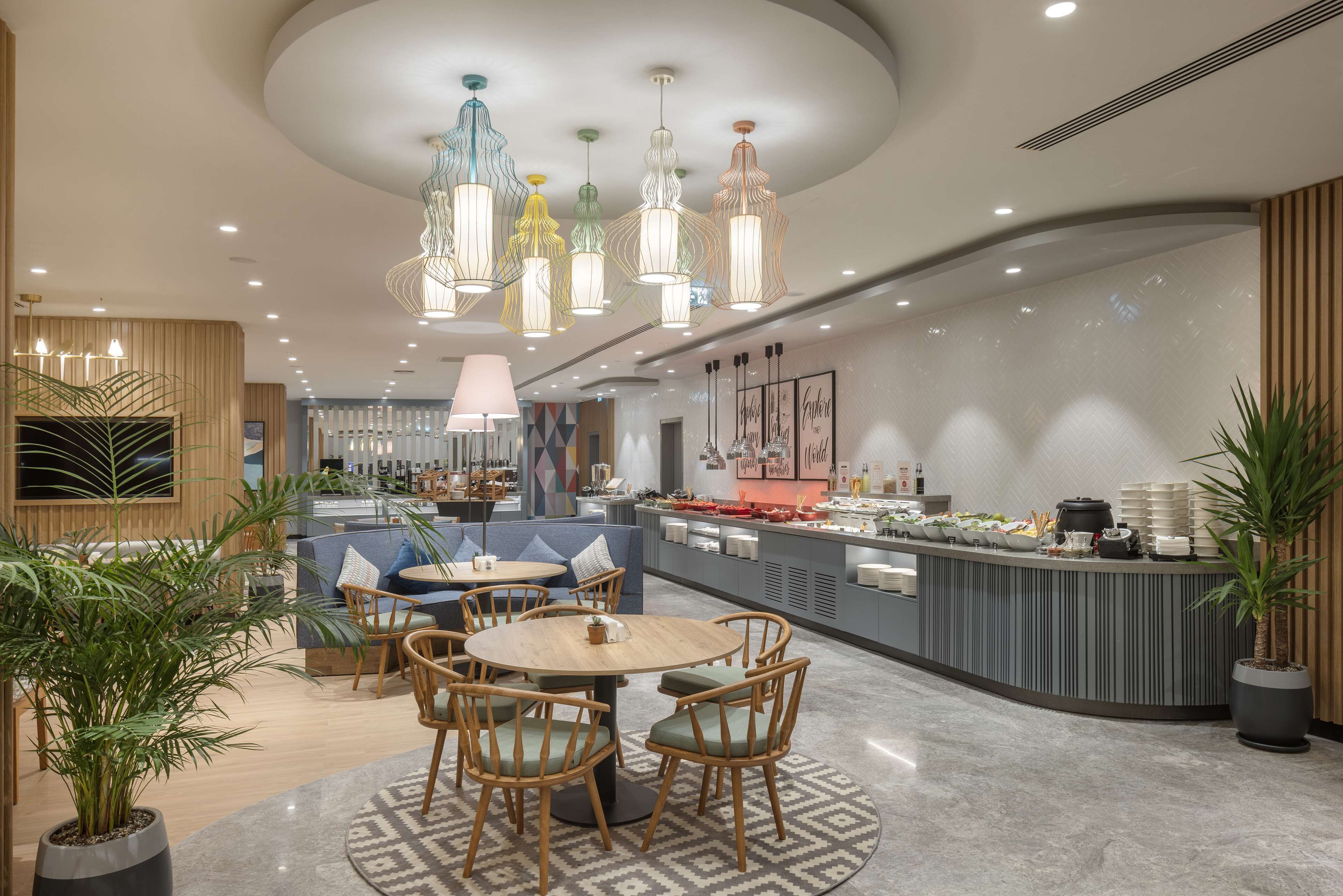 Un moderno vestíbulo de hotel con un área de estar central, un mostrador de recepción y varios elementos de iluminación.