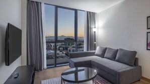 Een moderne woonkamer met een grijze modulaire bank, een glazen salontafel, een flatscreen-tv en een groot raam met uitzicht op de stad.