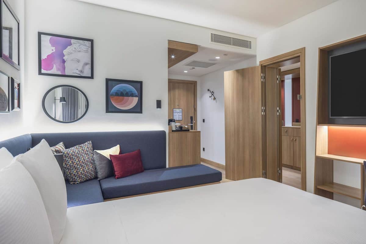 Een moderne hotelkamer met een bed, een sofa, een televisie en kunstwerken aan de wanden.