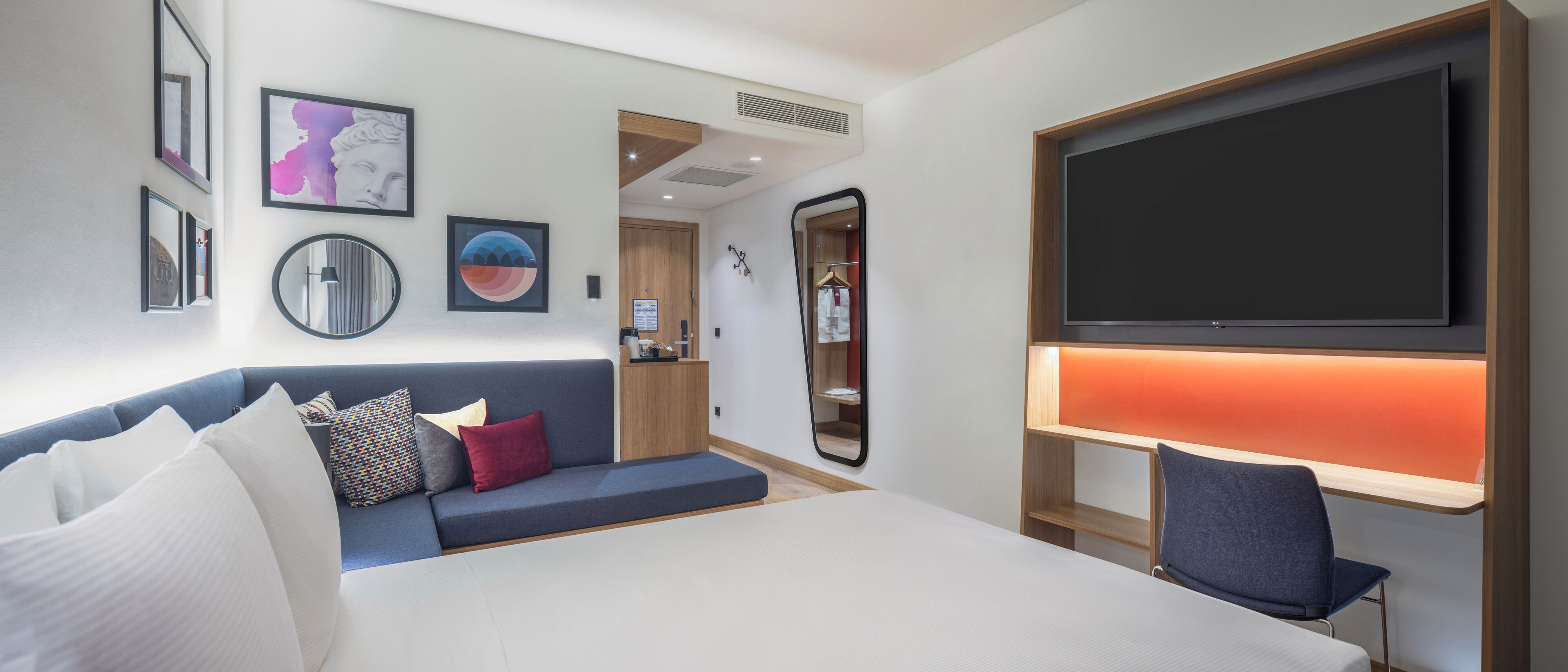 Ein modernes Hotelzimmer mit Bett, einer Sitzecke, einem Fernseher und Kunstwerken an den Wänden.