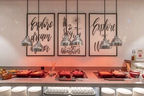 Ein reichhaltiges Buffet mit verschiedenen Speisen und Geschirr, dazu inspirierende Poster an den Wänden und hängende Pendelleuchten.