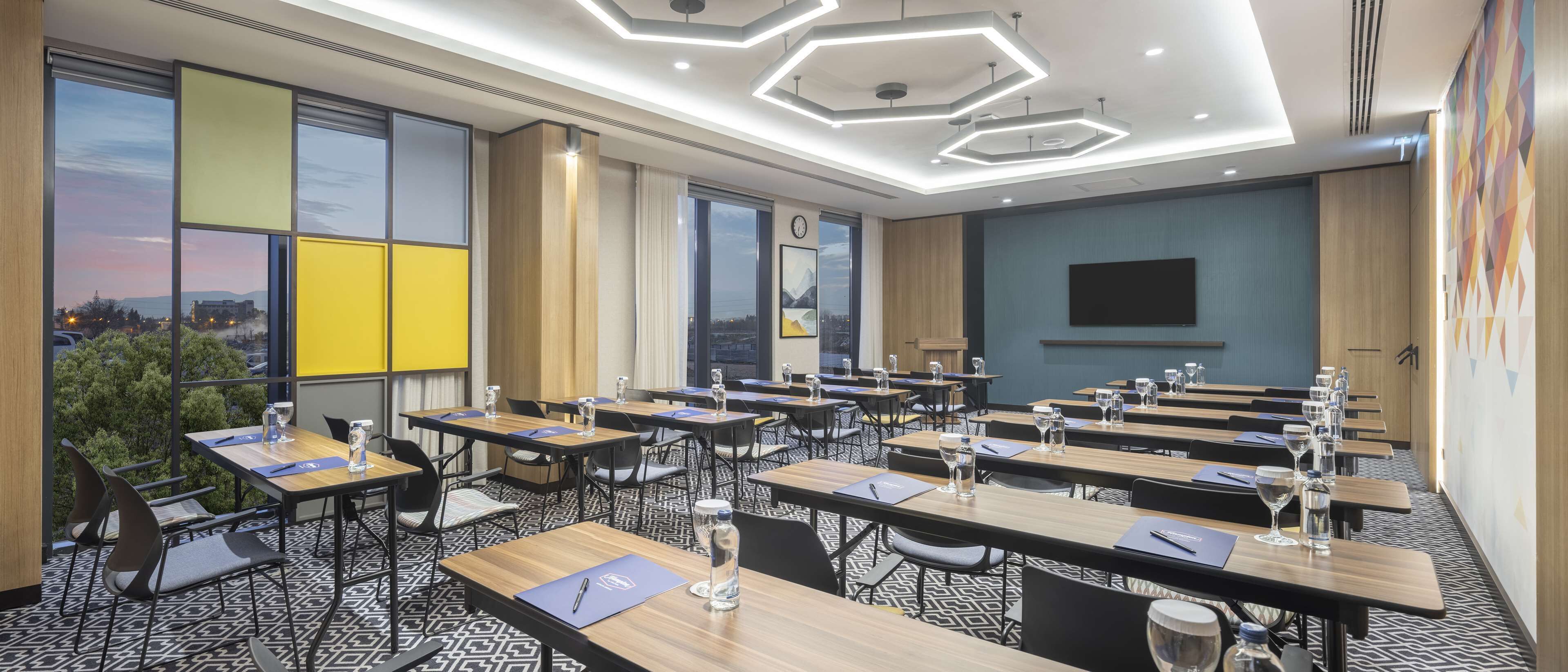 A conference room with multiple tables, chairs, and a large window offering a city view.