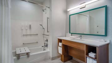 Un baño moderno con ducha envuelta en vidrio, tocador de madera con espejo y un pequeño taburete.