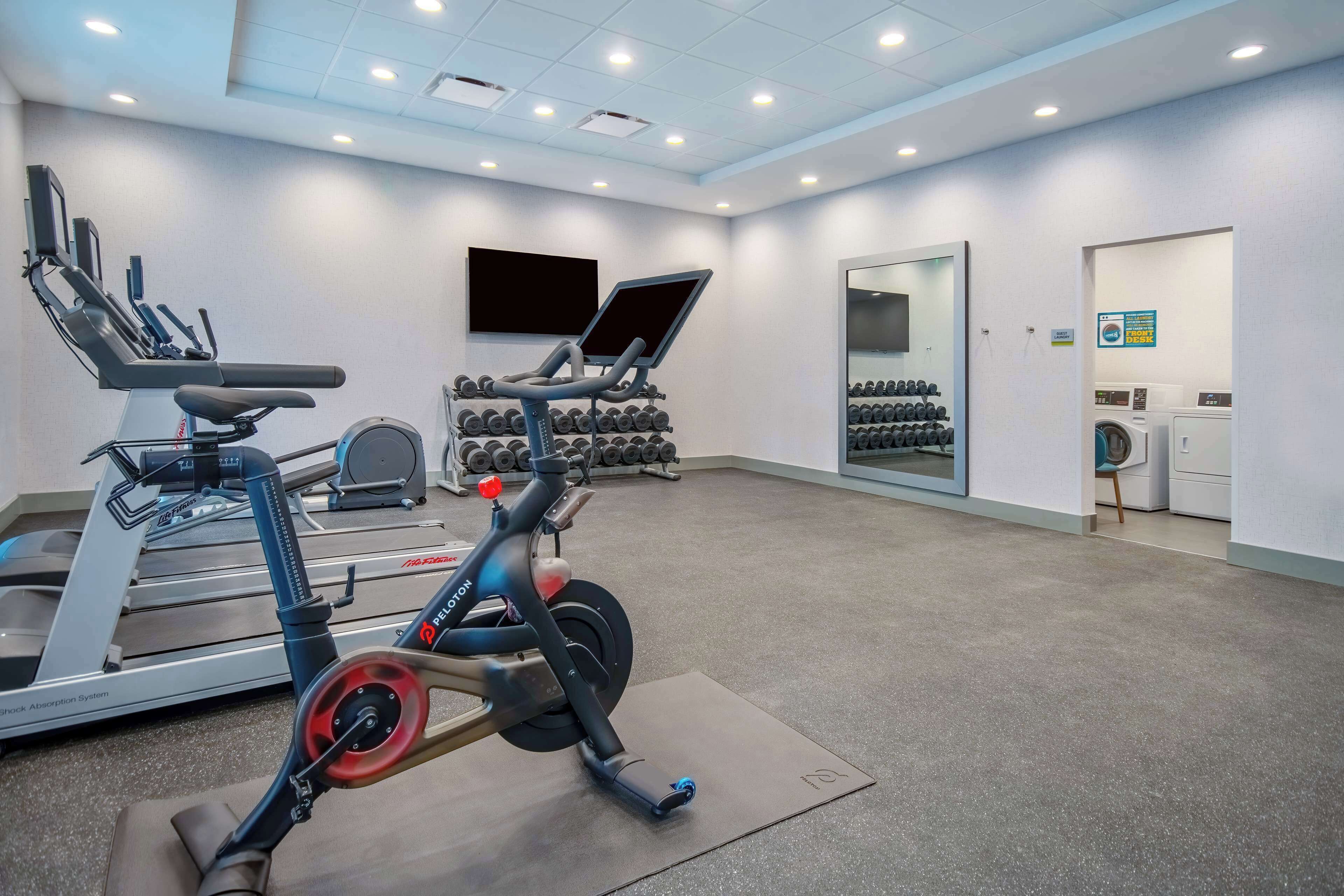 Un gimnasio con equipo de cardio, mancuernas y un espejo.