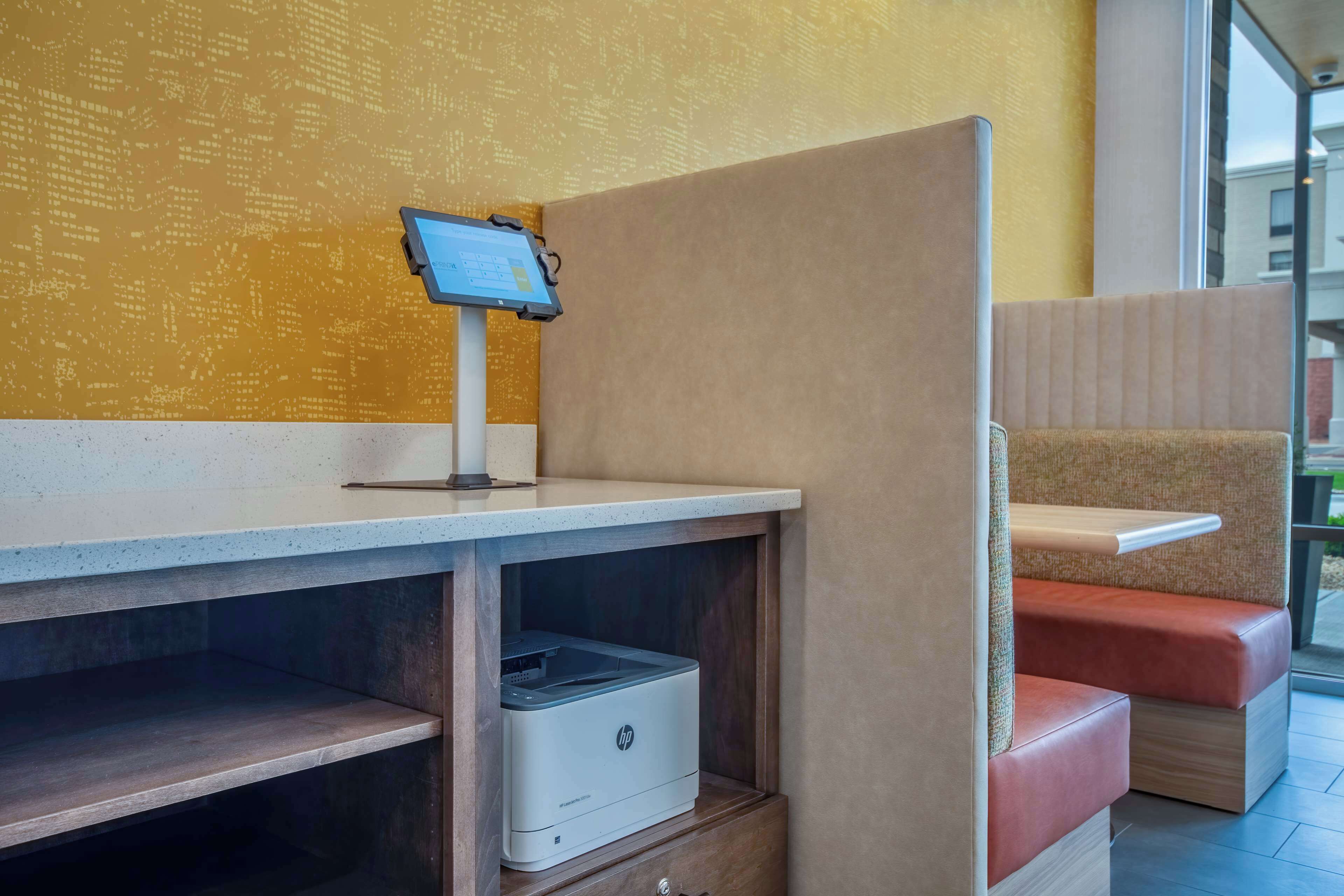 Un área de descanso con un quiosco digital, una impresora y un banco acolchado.