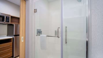 A modern bathroom with a glass shower enclosure, a stainless steel refrigerator, and a wooden cabinet.