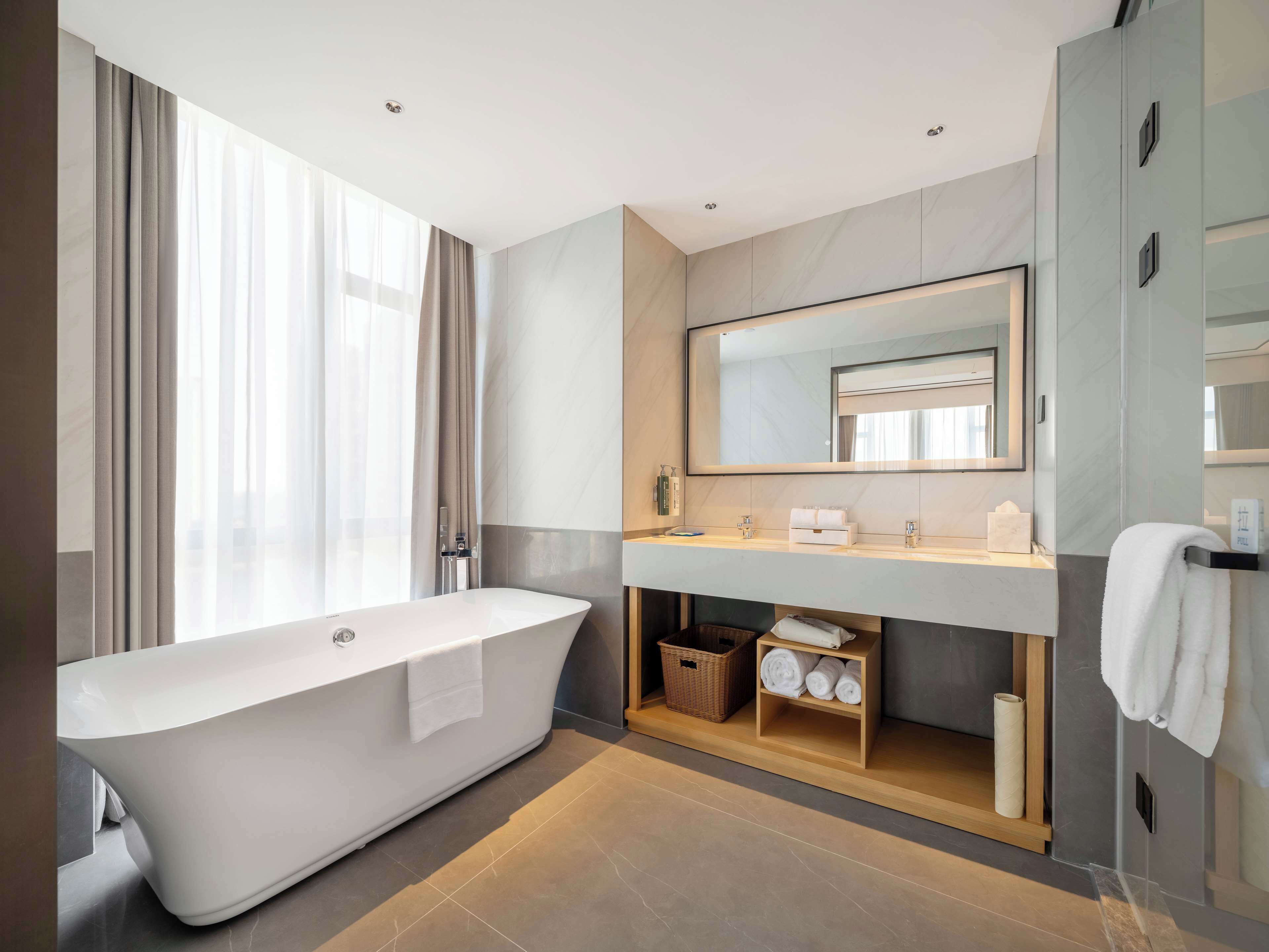 A modern bathroom with a freestanding bathtub, a large mirror, and a vanity with a towel rack.