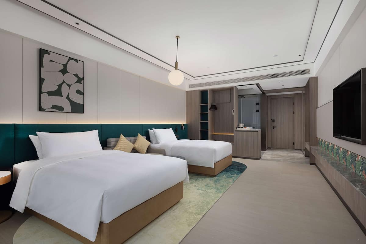 A modern hotel room with two beds, a TV, and a bathroom visible through an open door.
