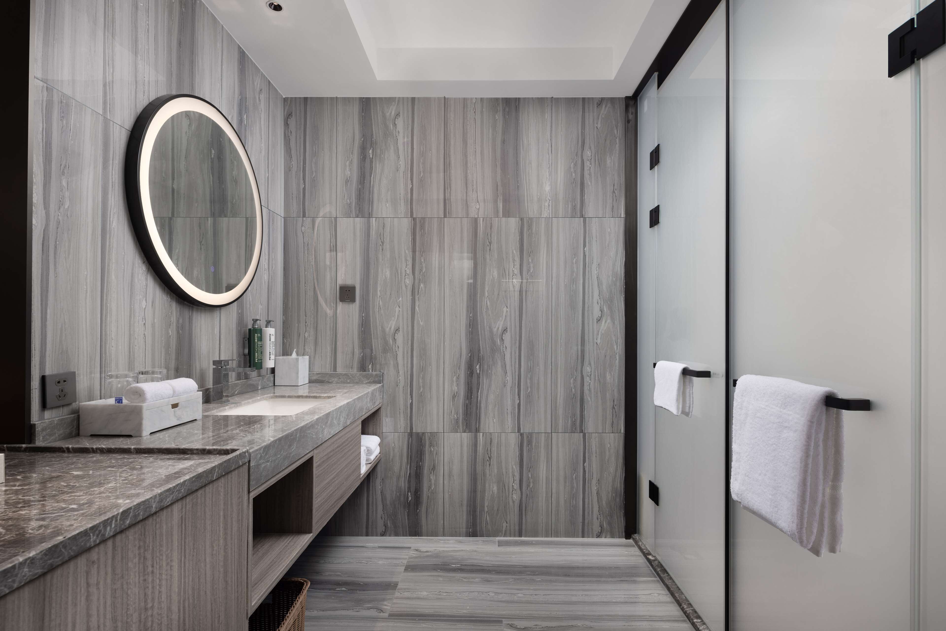 A modern bathroom with a marble vanity, a large mirror, and a towel rack.