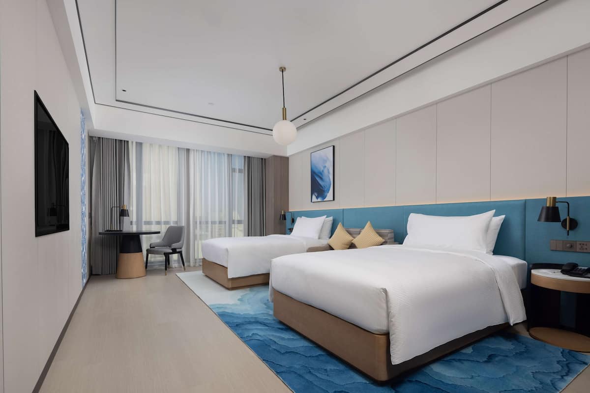A modern hotel room with two beds, a desk, and a chair.