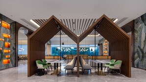 Een modern interieur met een centrale zithoek, houten scheidingswanden en uitzicht op groen door grote ramen.