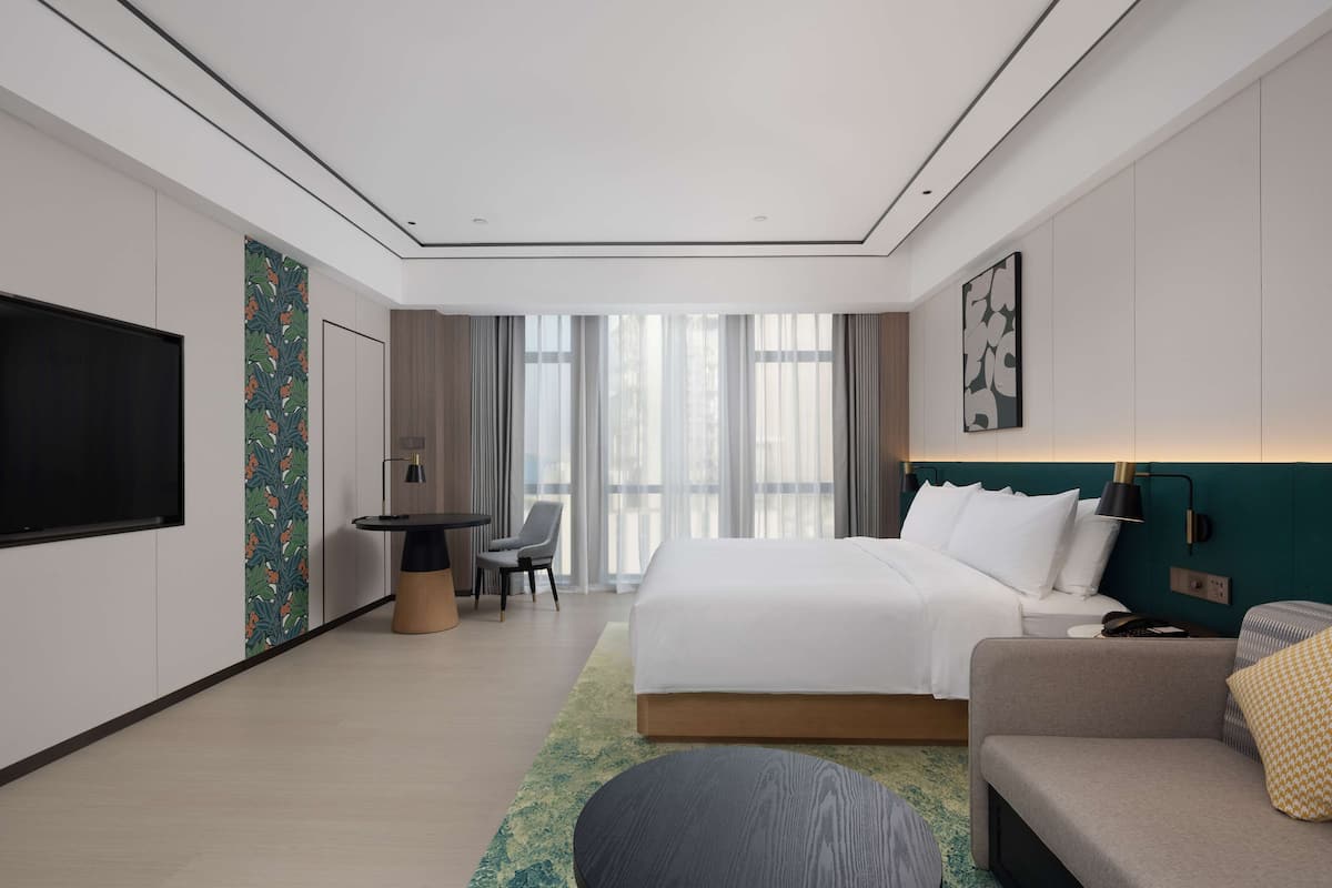 A modern hotel room with a large bed, a desk, a chair, and a TV.