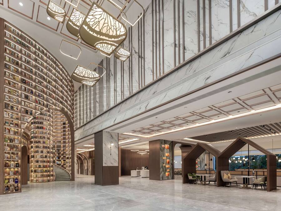 Een ruime lobby met een centrale trap, een grote boekenkast en een receptiebalie.