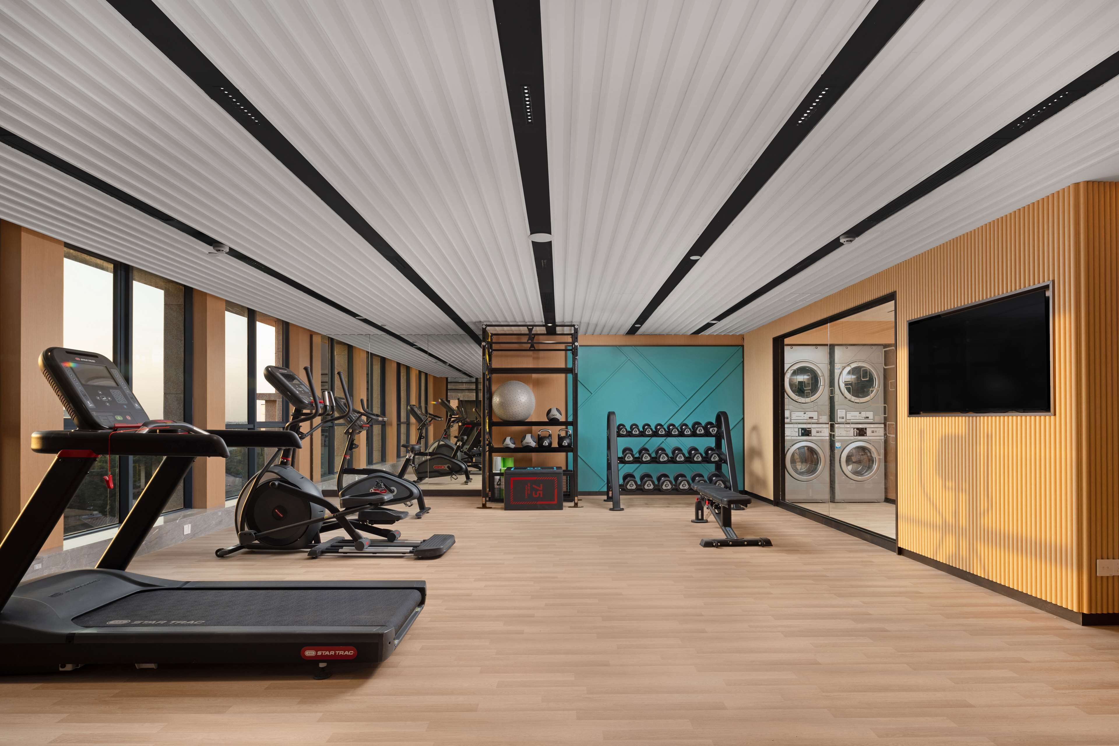 A gym with treadmills, elliptical machines, and a wall-mounted TV.