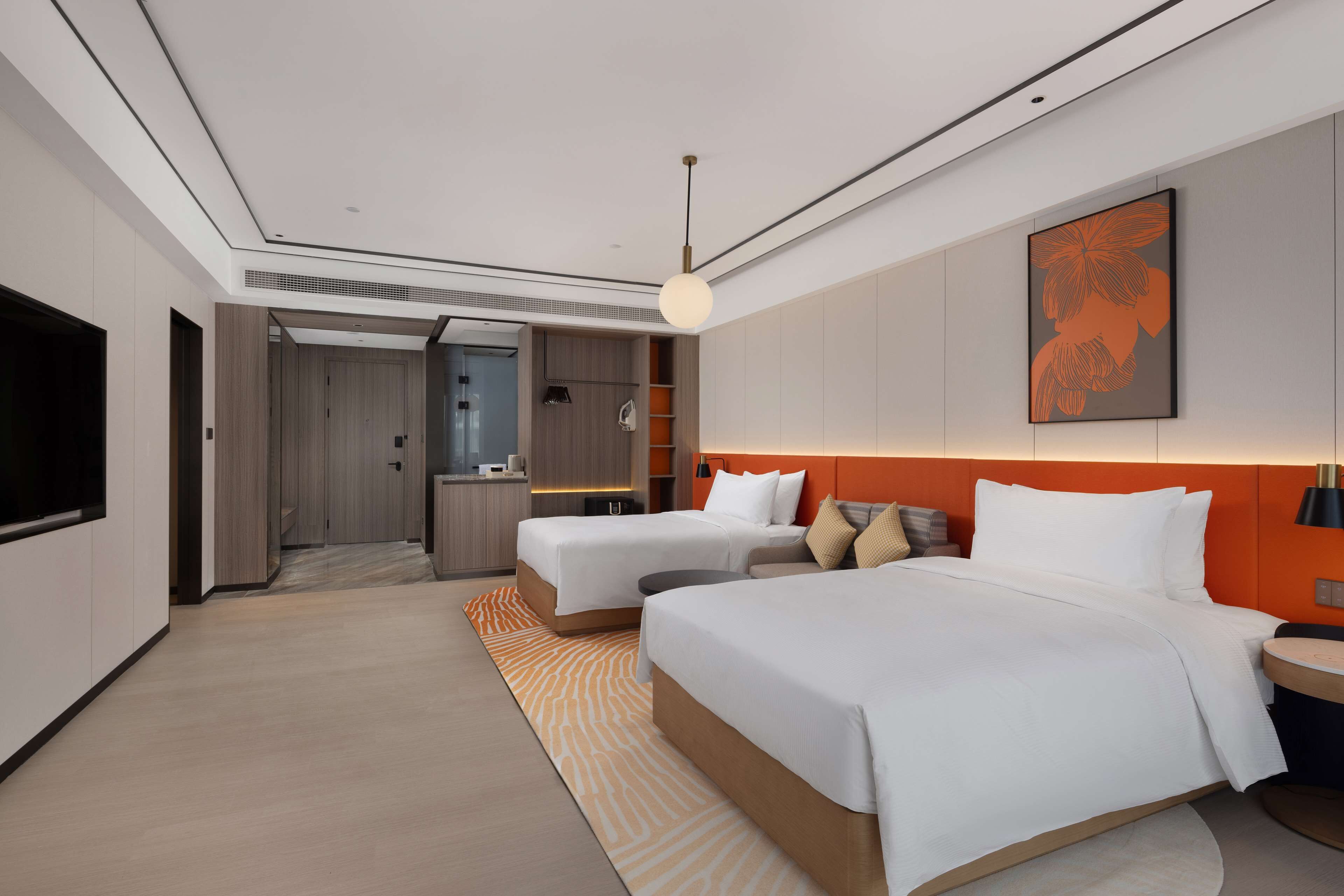 A modern hotel room with two beds, a TV, a desk, and a bathroom visible through an open door.