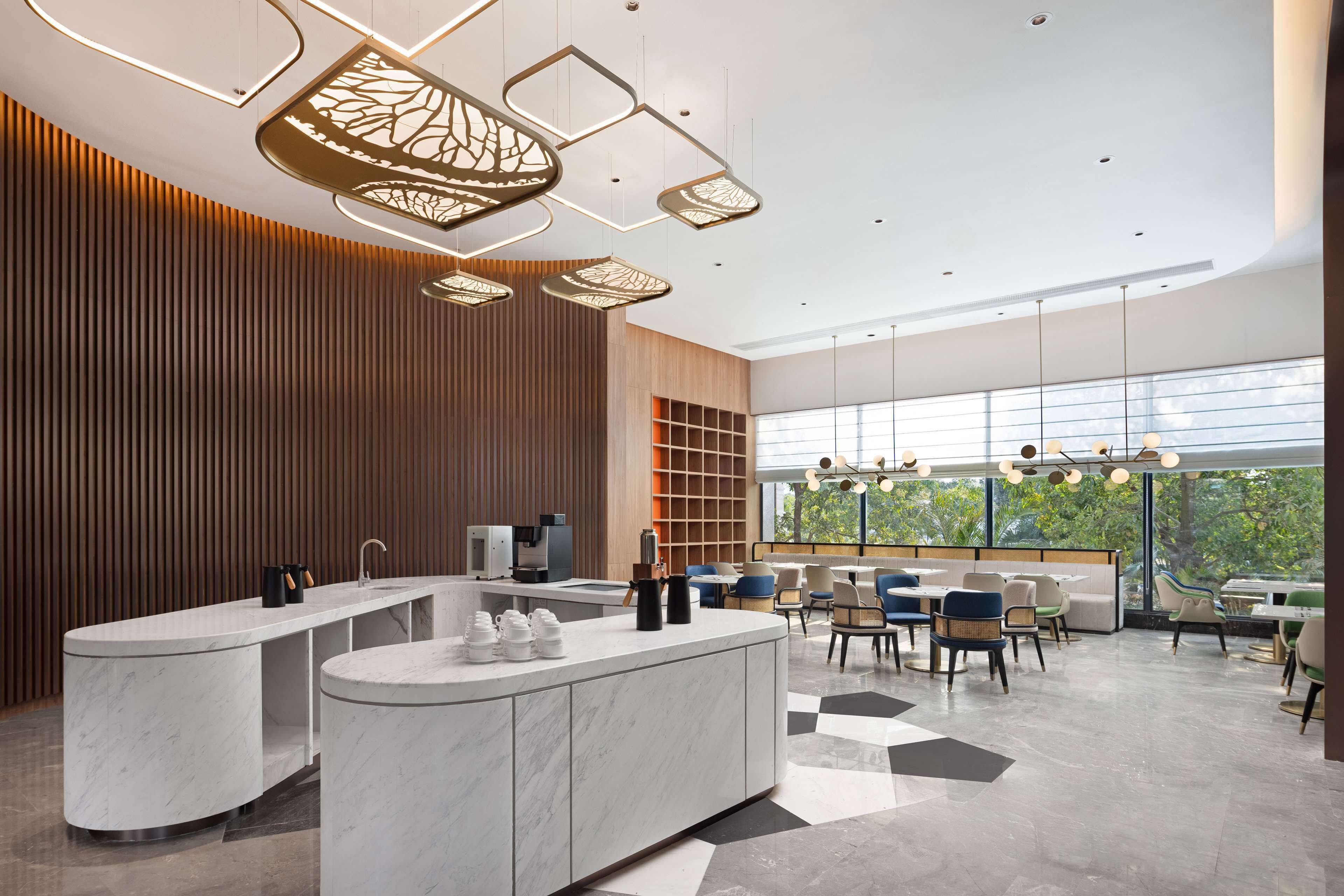 A modern hotel lobby with a marble reception desk, seating area, and large windows offering a view of the outdoors.