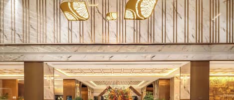 A spacious lobby with a marble floor, a central floral arrangement, and modern lighting fixtures.