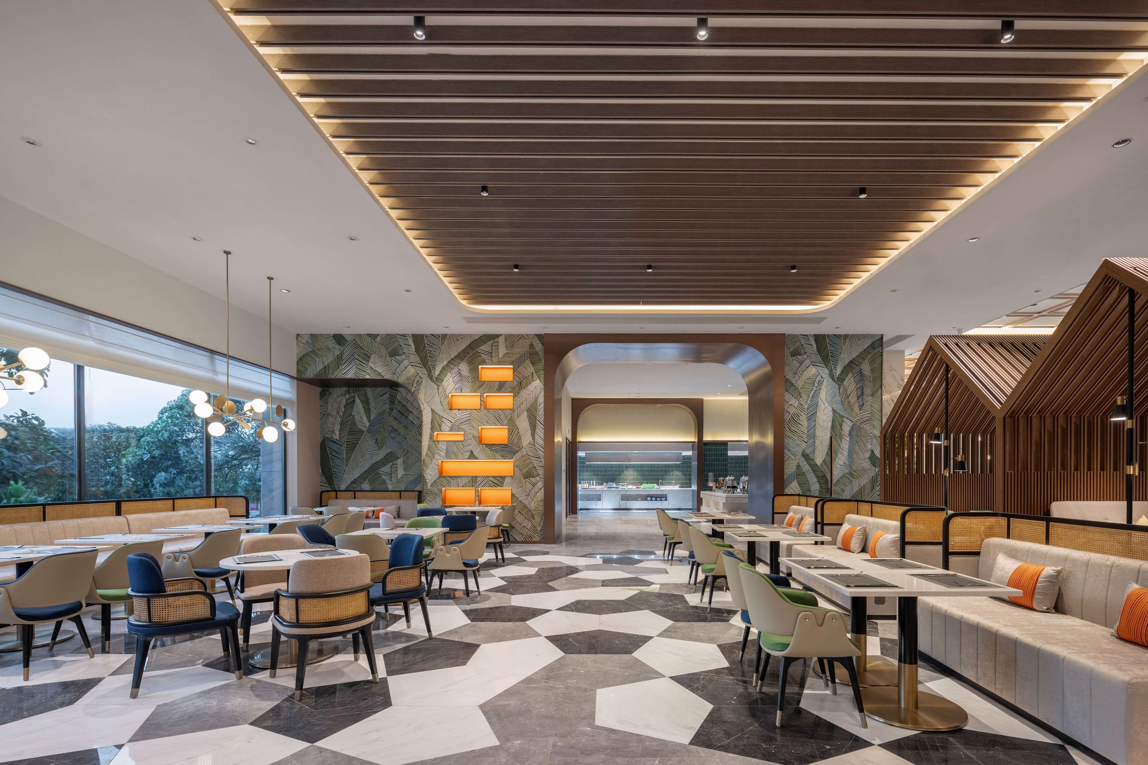 Un hall d’hôtel moderne avec un sol à carreaux, des coins salon et, au fond, une vue sur la cuisine.