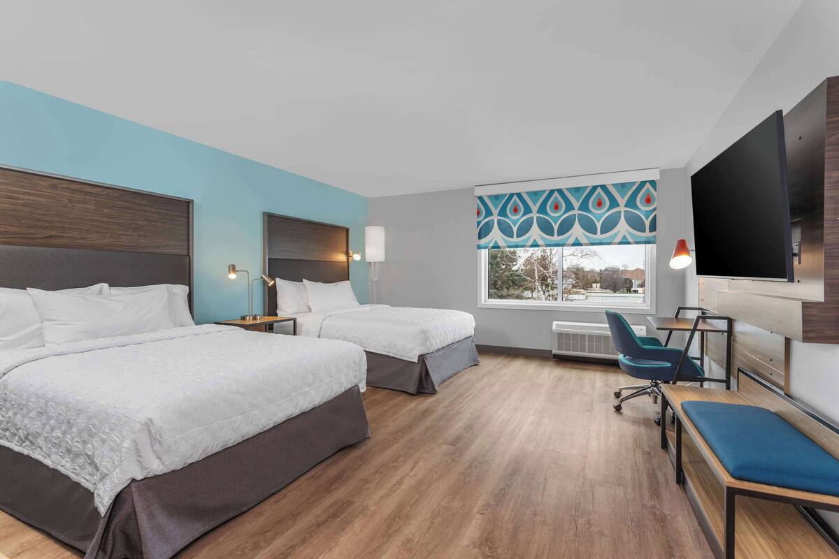 Une chambre d’hôtel avec deux lits, un bureau, une chaise et une télévision.