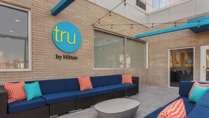 An outdoor seating area with a blue sofa and a round table, a sign reading "tru by Hilton", and a brick wall.