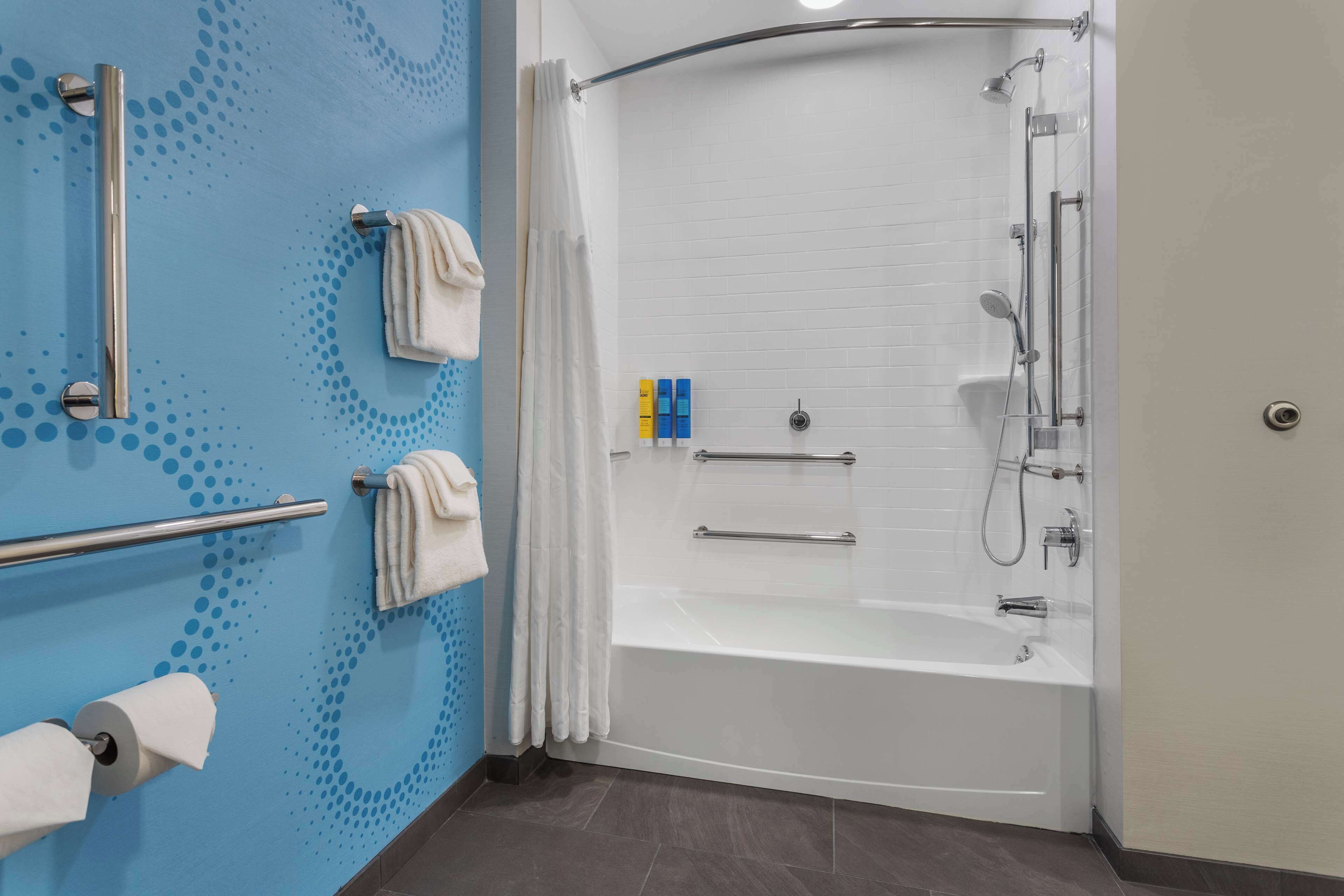 Un baño moderno con ducha, barras de apoyo, un perchero para toallas y un soporte para papel higiénico.