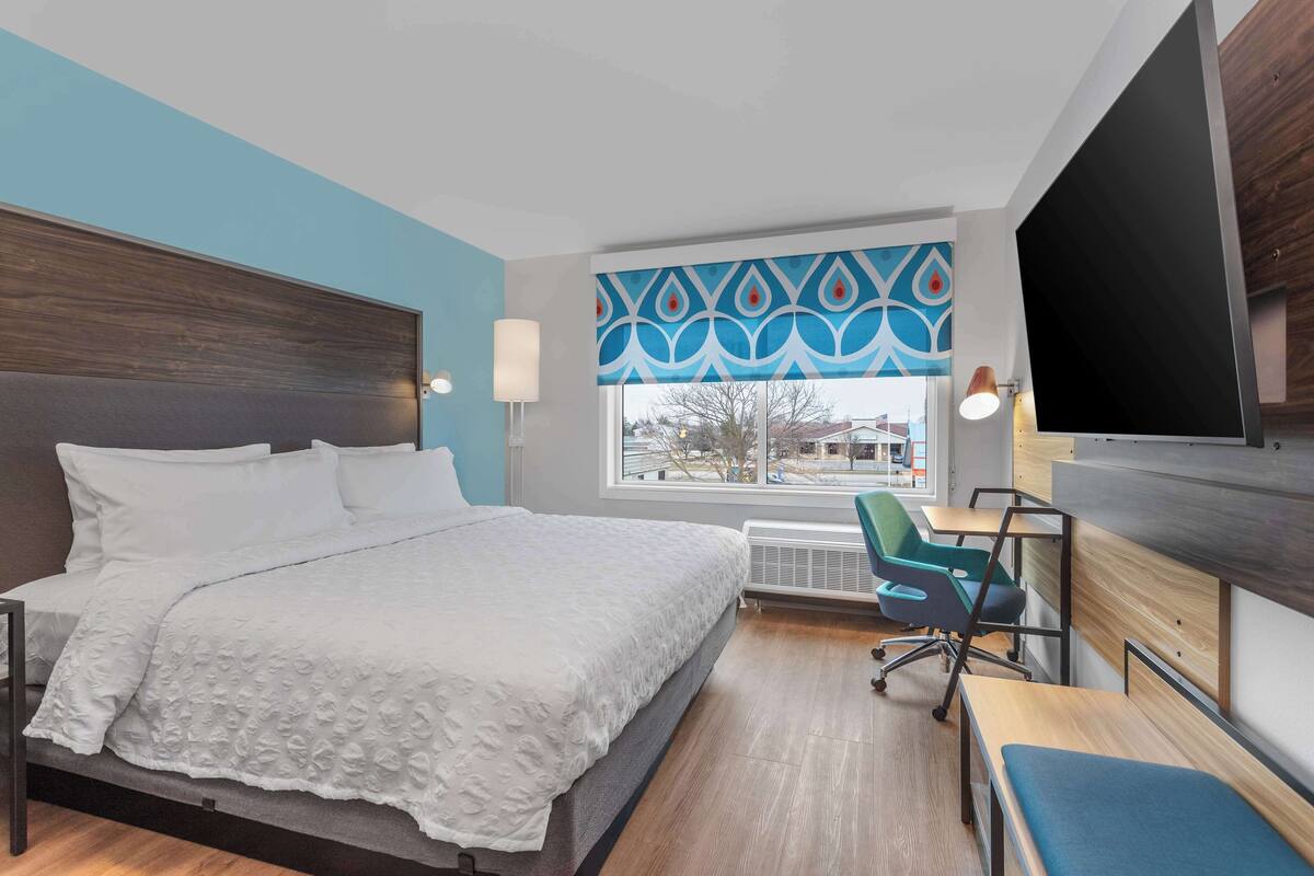 Une chambre d’hôtel avec un grand lit, un bureau avec une chaise, une télévision et une fenêtre donnant sur l’extérieur.