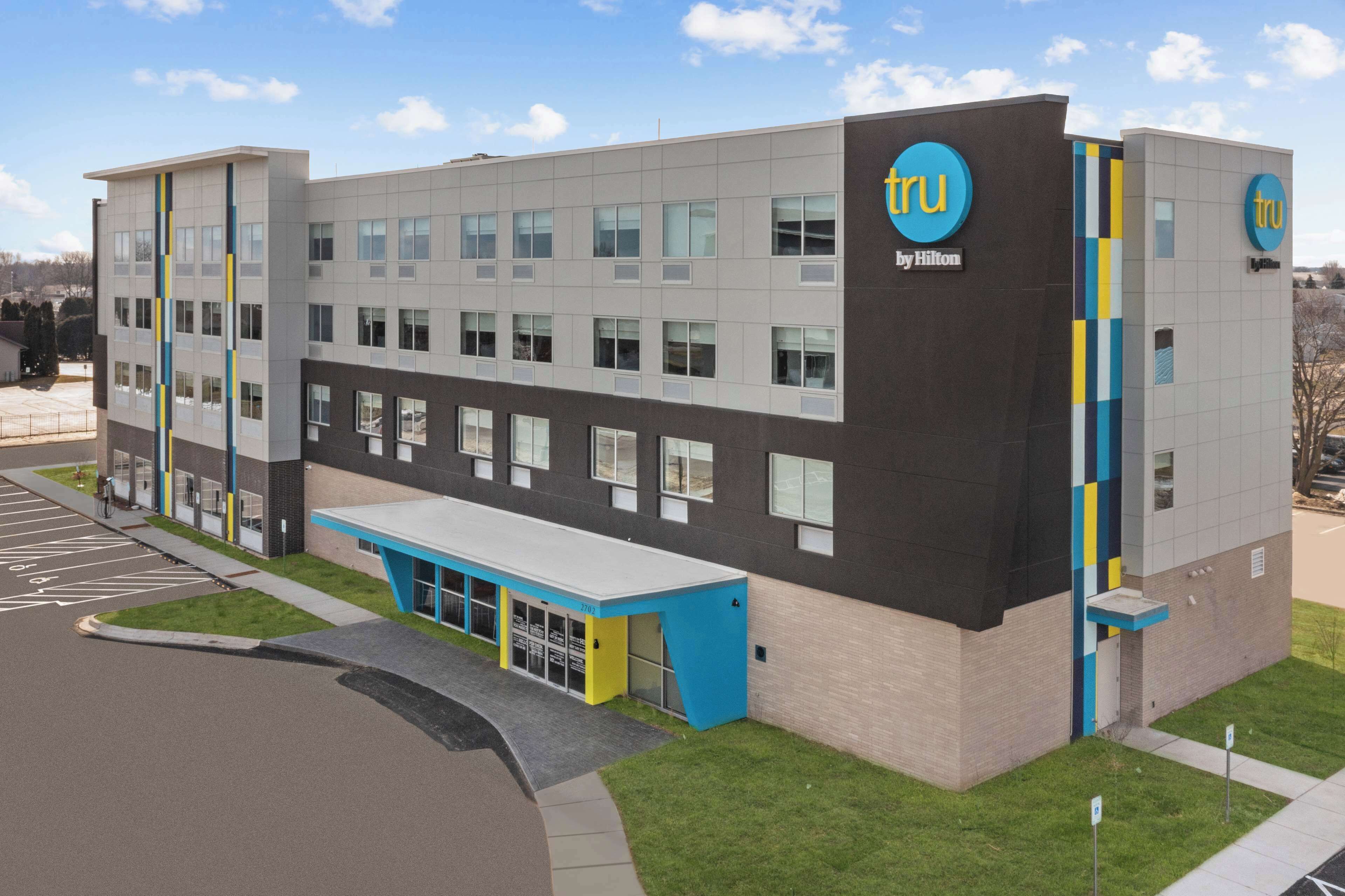 A modern hotel building with a flat roof, large windows, and a blue and yellow entrance.