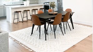 A modern kitchen with white cabinets, a central island, and a dining area with a round table and chairs.