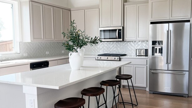 A modern kitchen with white cabinetry, a stainless steel refrigerator, a microwave, and a large island with bar stools.