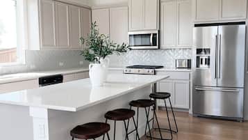 A modern kitchen with white cabinetry, a stainless steel refrigerator, a microwave, and a large island with bar stools.
