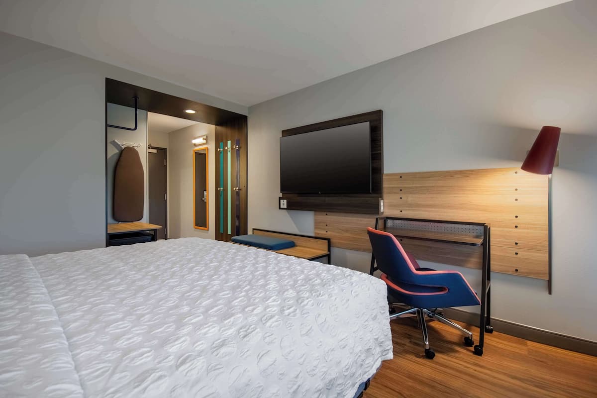 Une chambre d’hôtel moderne dotée d’un grand lit, d’un bureau avec une chaise, d’une télévision à écran plat et d’un miroir.