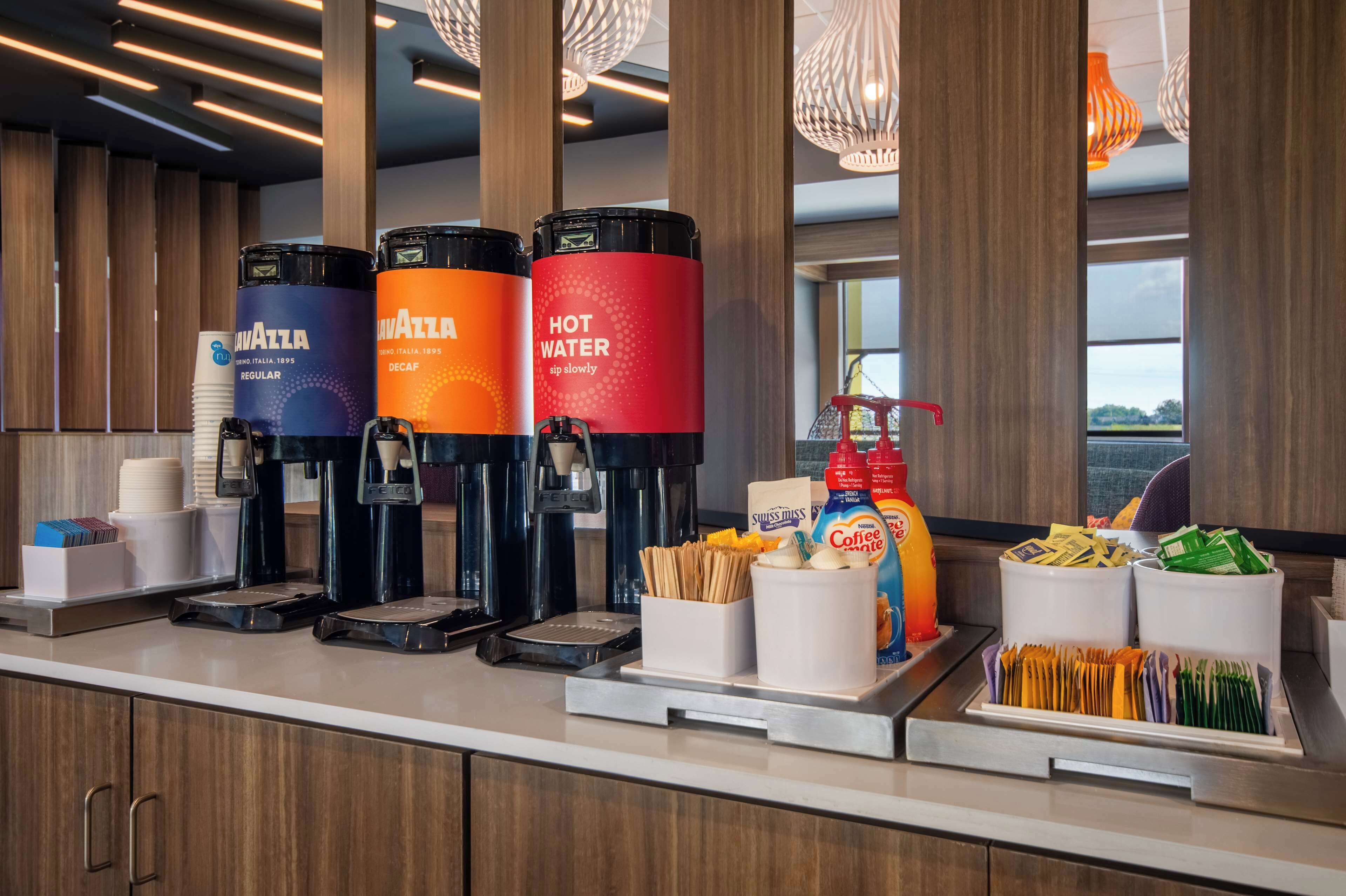 A coffee station with three dispensers labeled 'Mavazza' and 'Hot Water', along with various coffee pods and utensils.