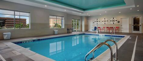 An indoor swimming pool with clear water, tiled flooring, and a ceiling with a teal accent.