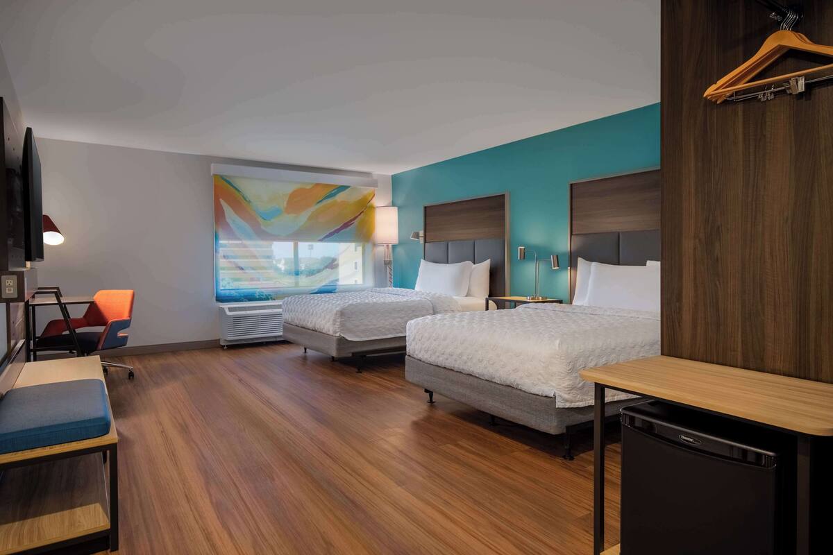 Une chambre d’hôtel avec deux lits, un bureau, une chaise, une télévision et une fenêtre donnant sur un paysage coloré.