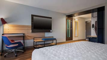 A modern hotel room with a bed, a desk with a chair, a TV mounted on the wall, and a shower area.