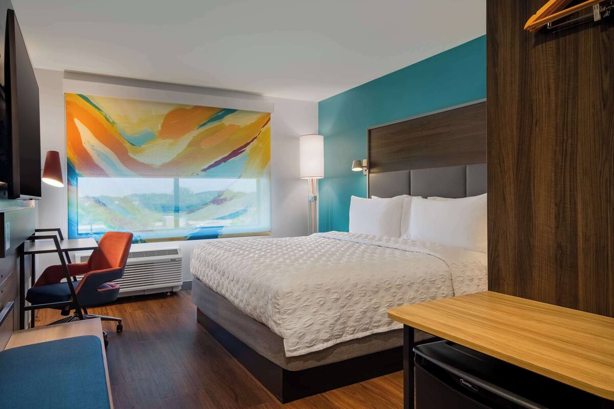 Une chambre d’hôtel moderne dotée d’un grand lit, d’un bureau, d’une chaise, d’une télévision et d’une fenêtre offrant une vue agréable.