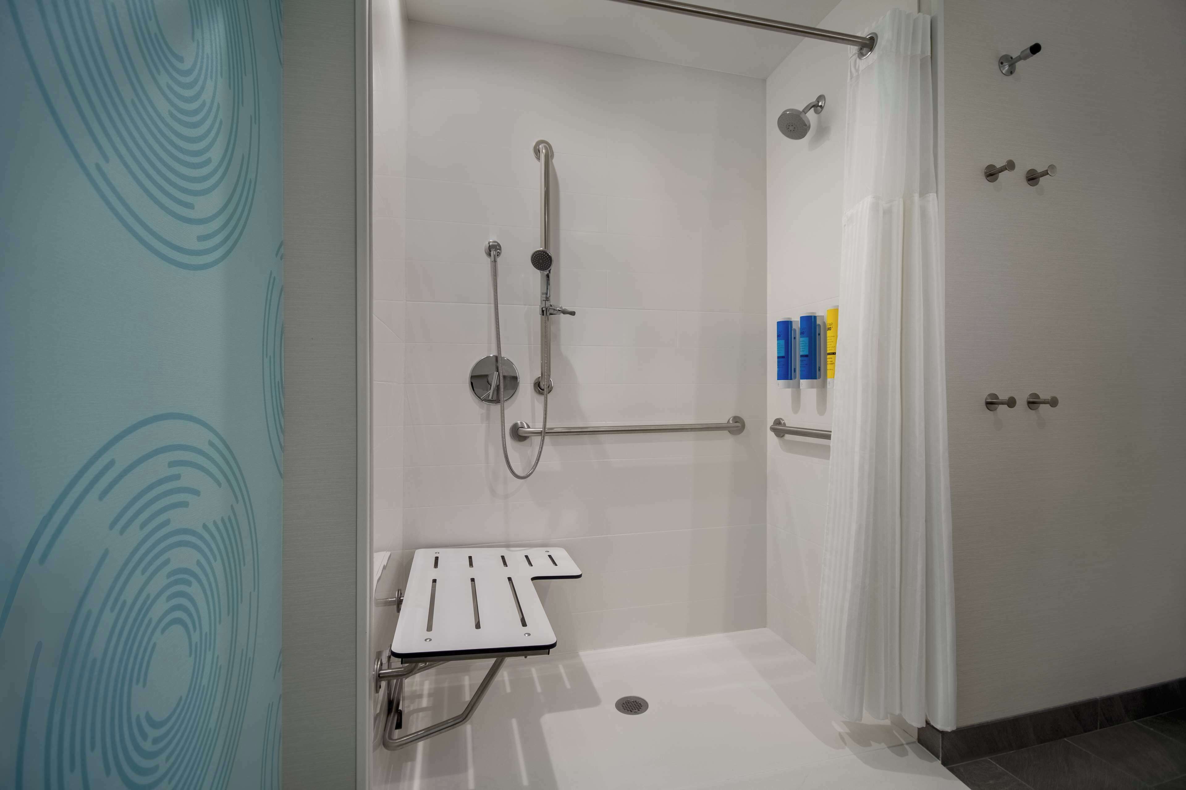 Un espace douche moderne équipé d’une barre d’appui, d’un pommeau de douche et d’un flexible de douche.