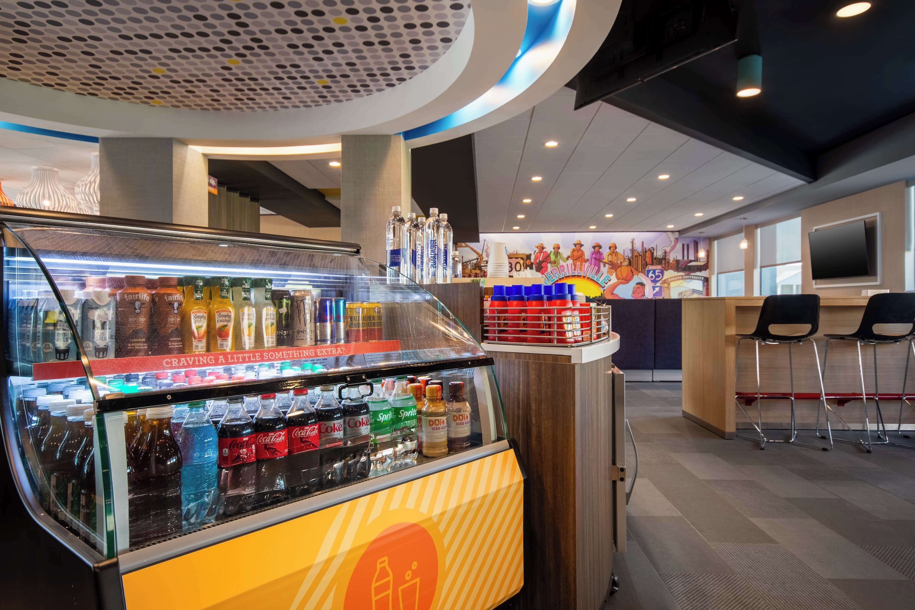Un distributeur automatique proposant diverses boissons, un comptoir orné d’une fresque murale et un espace détente avec des chaises.