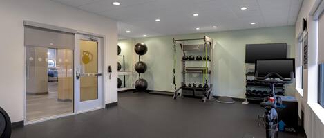 A gym with exercise equipment, a television, and a door leading to another room.