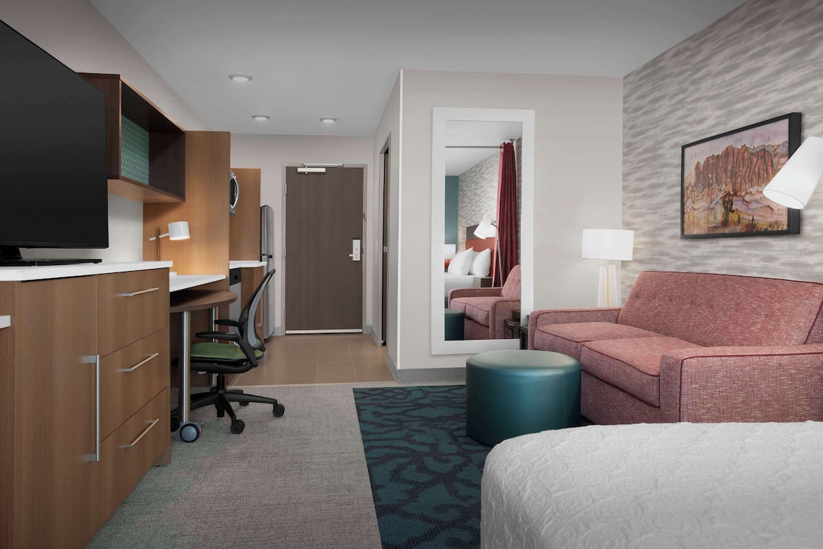 Ein Hotelzimmer mit einem Bett, einem Schreibtisch mit Computer, einem Fernseher und einem Sofa.